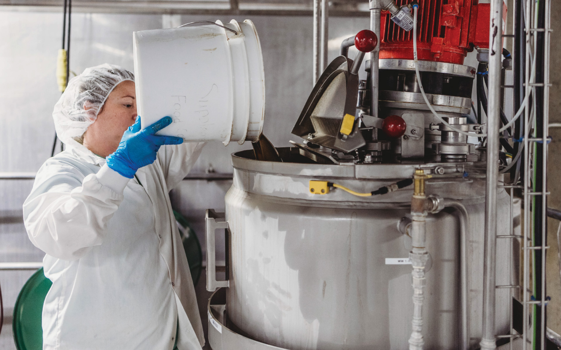photo of woman dumping ingredients from bucket into large vat